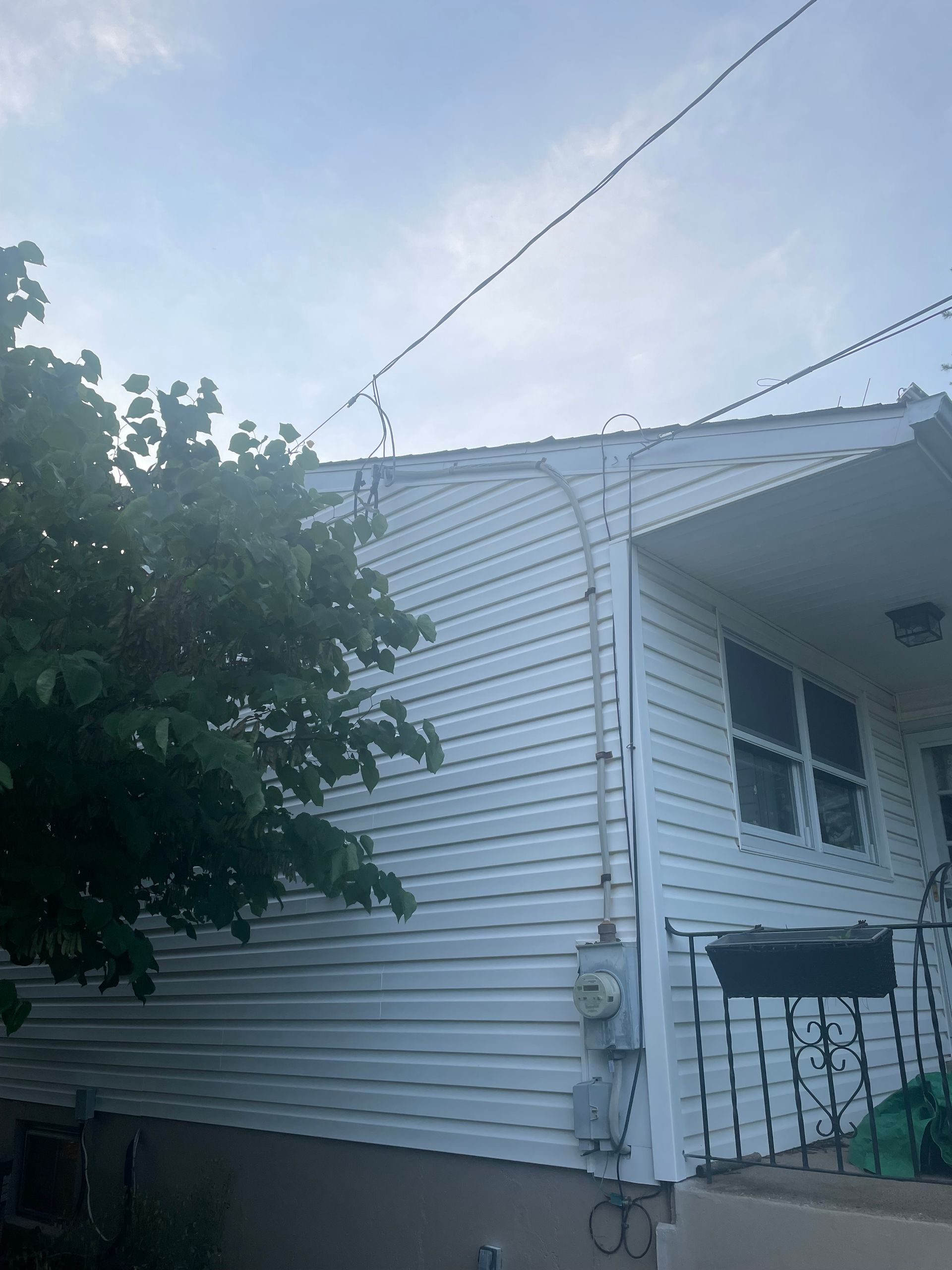 A white house with a porch and a tree in front of it.