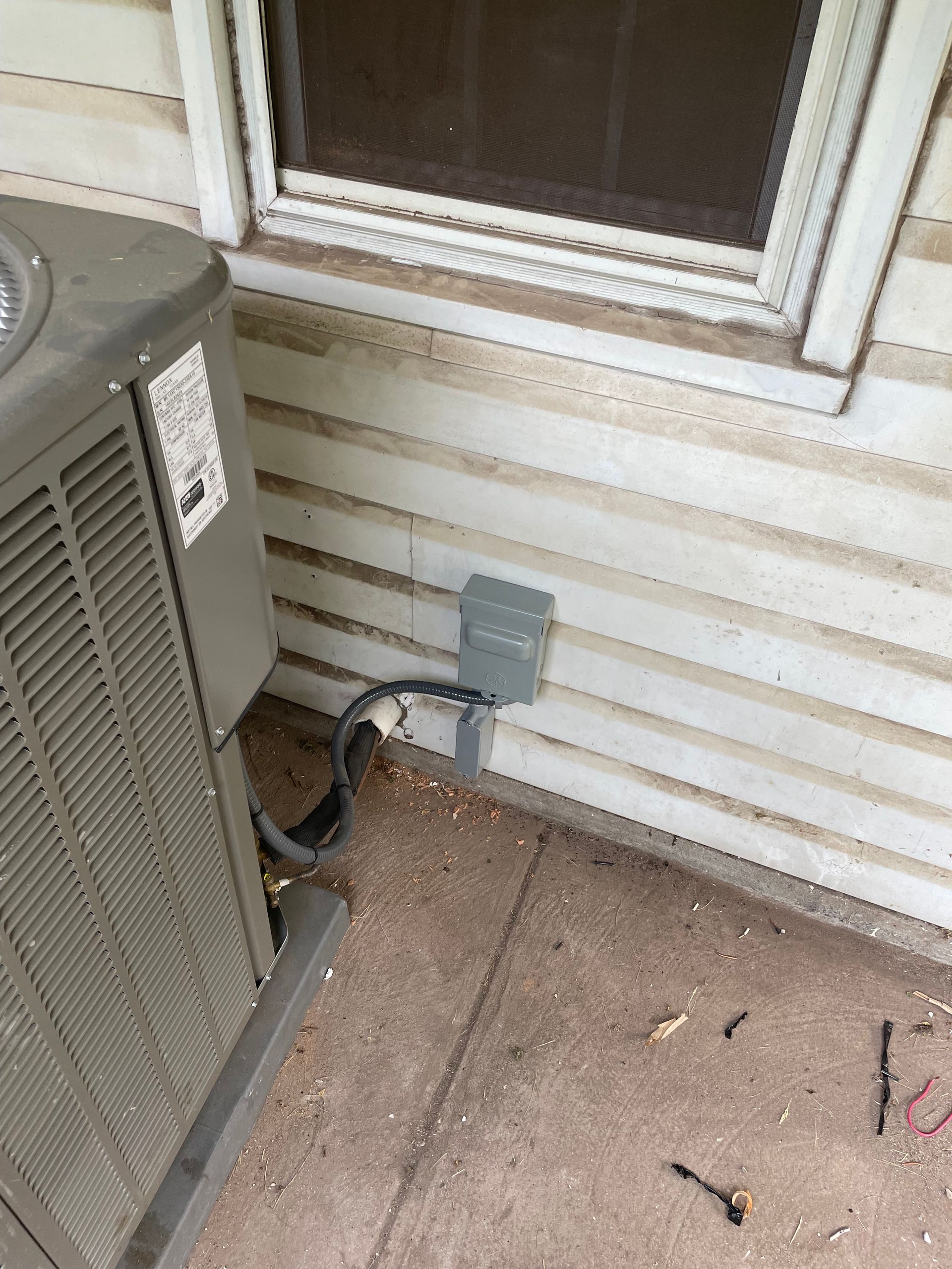 An air conditioner is sitting on the side of a house next to a window.