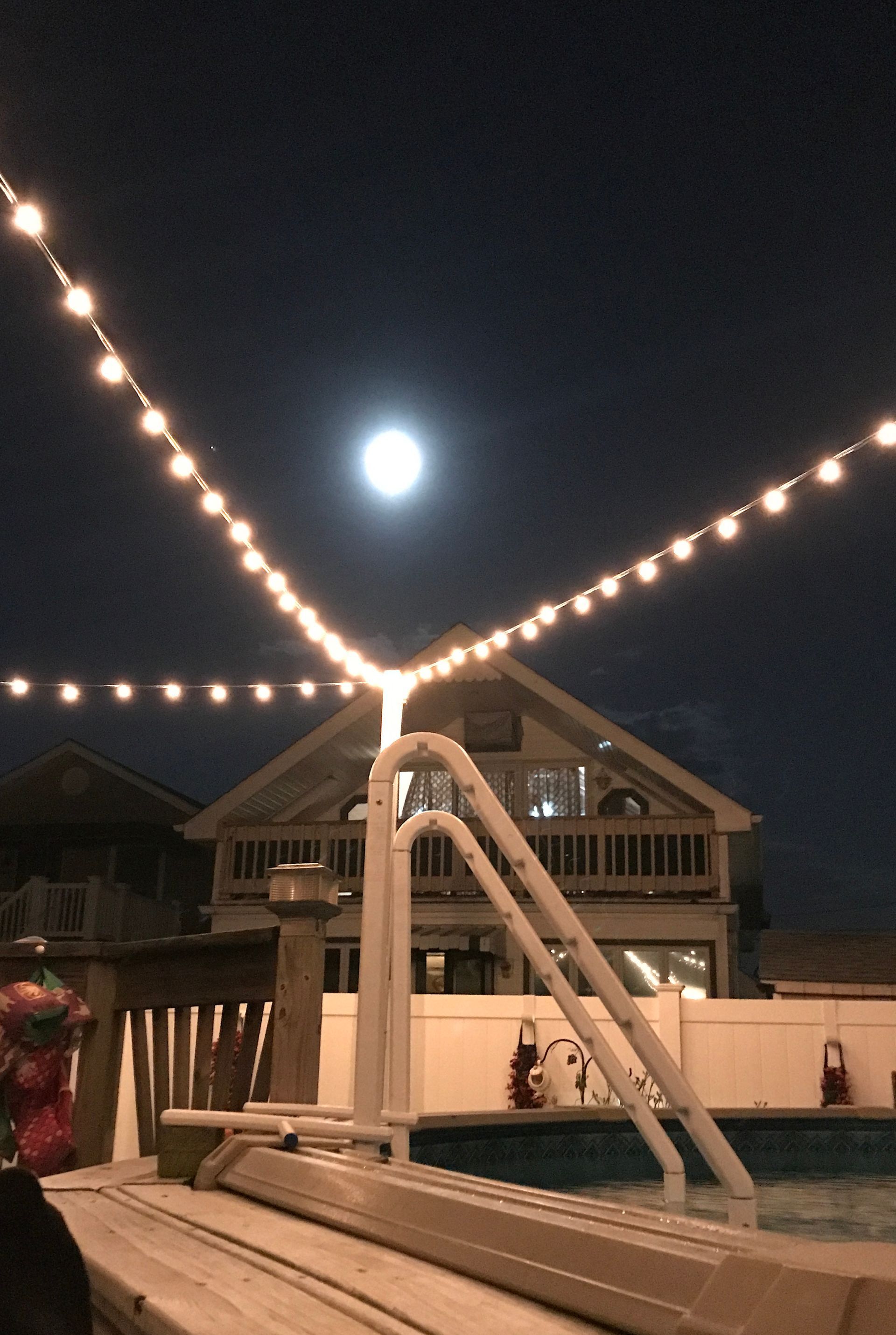 A swimming pool is lit up at night with a full moon in the background