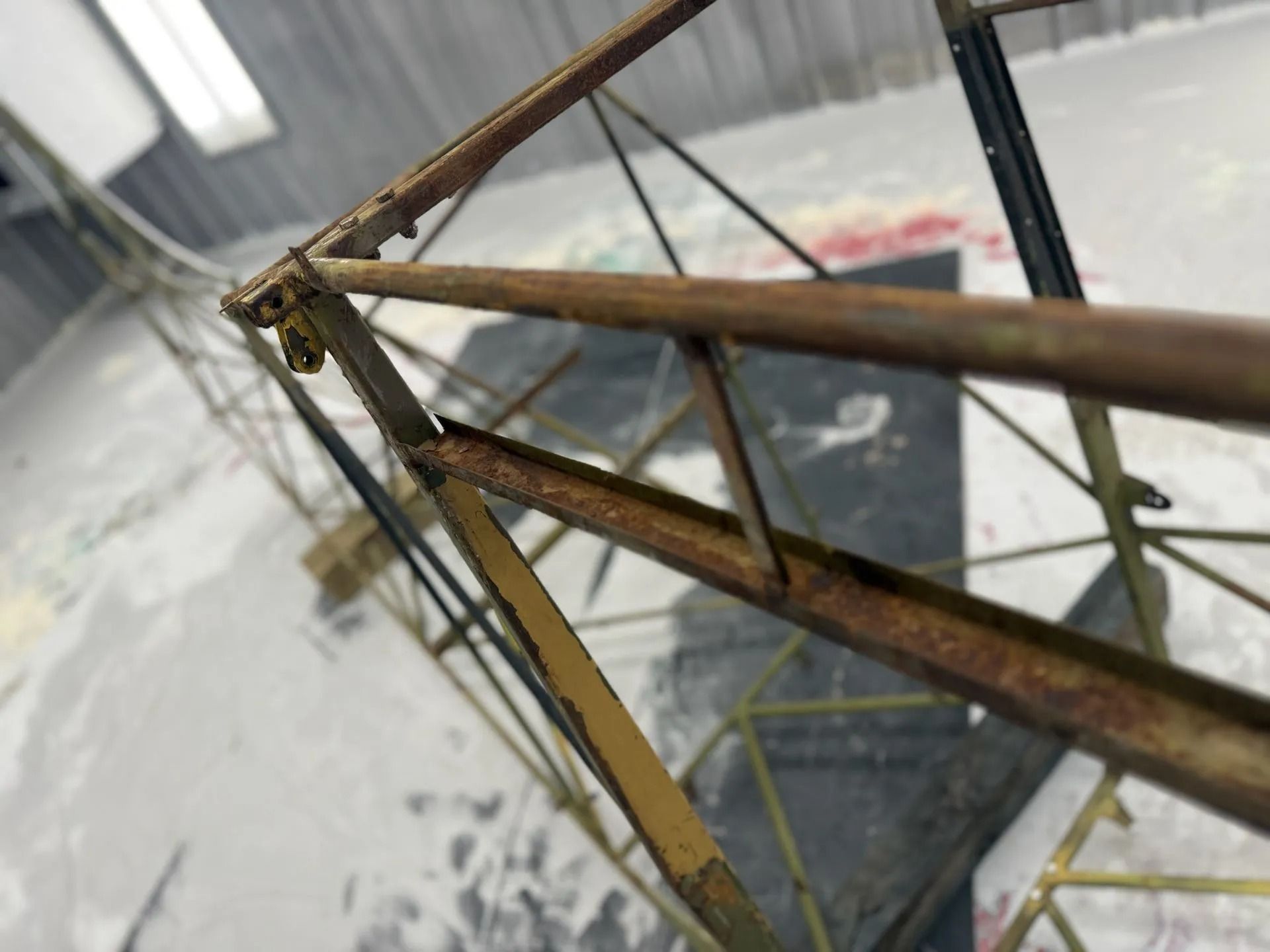 Close-up view of a rusty metal geometric frame structure, set against a concrete floor.