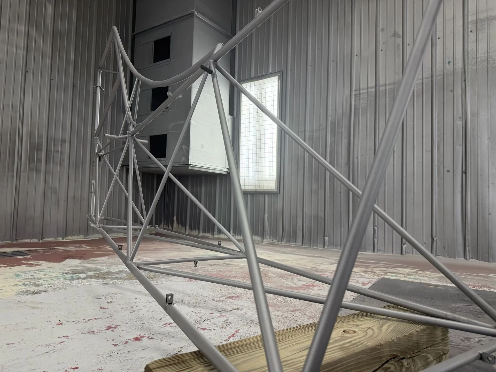 Steel frame being painted in a gray spray booth.