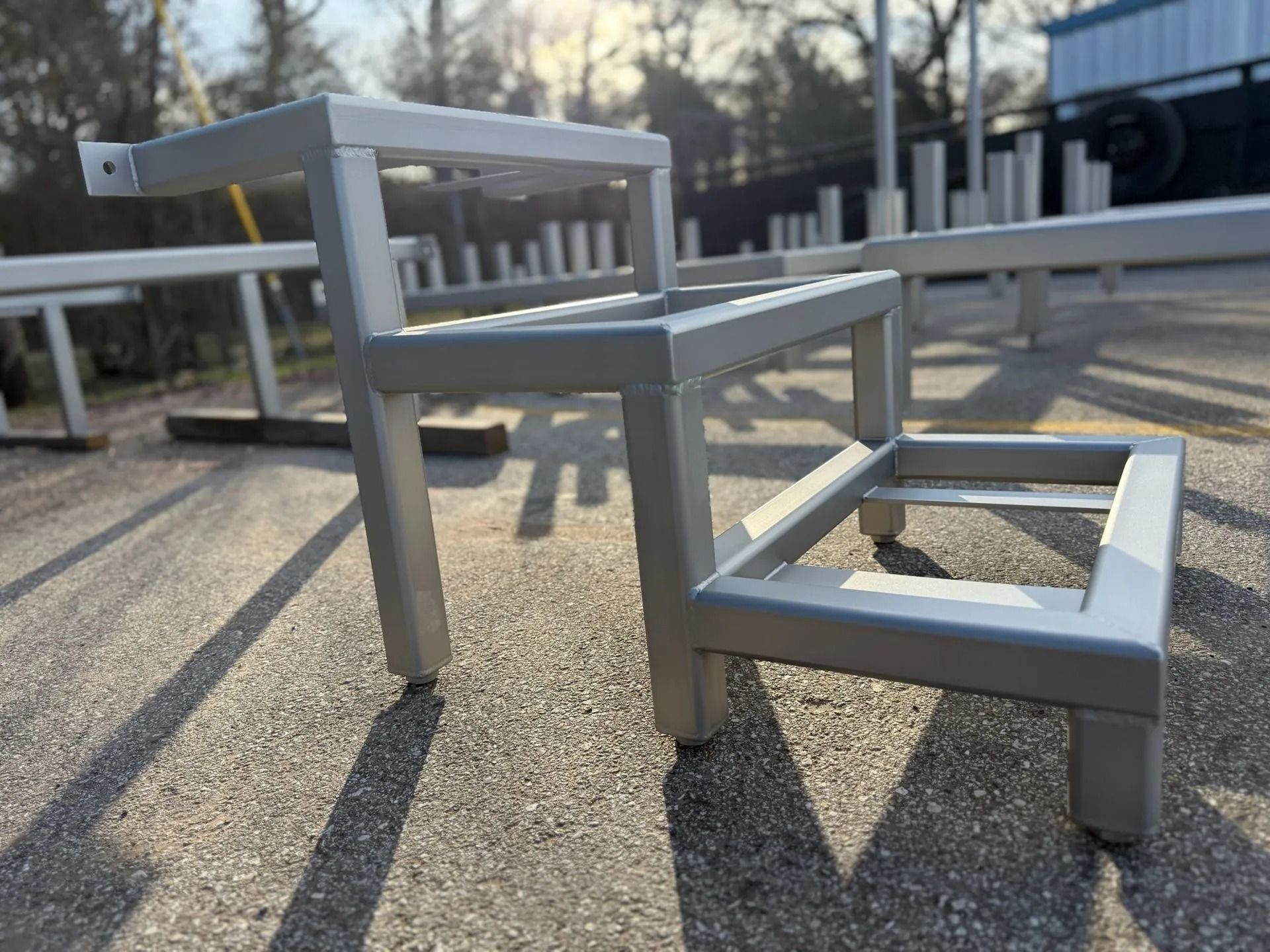 Silver metal step stool outdoors on asphalt. Three steps with square frames.