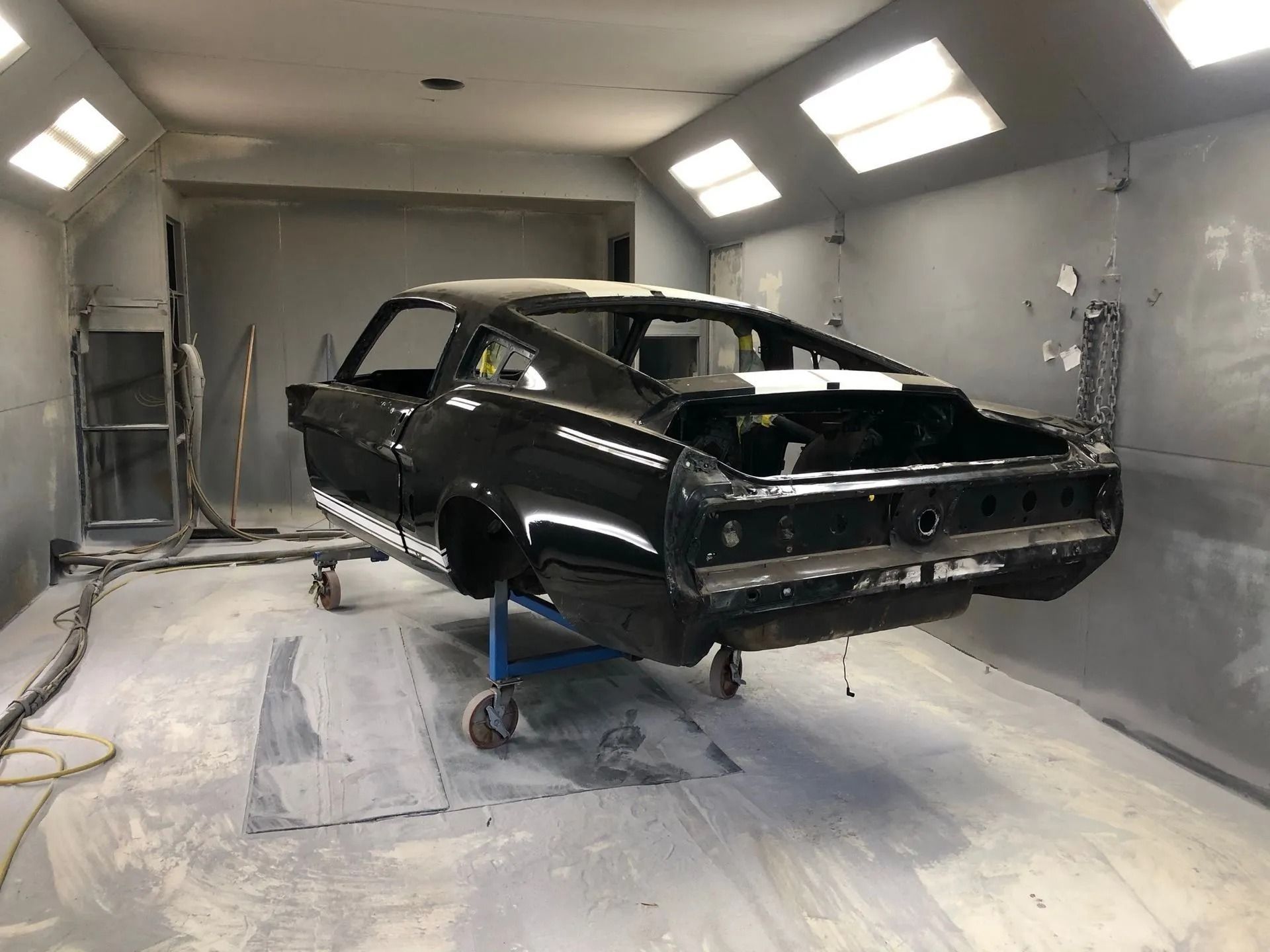 Black classic car in a paint booth on a lift; undergoing restoration.