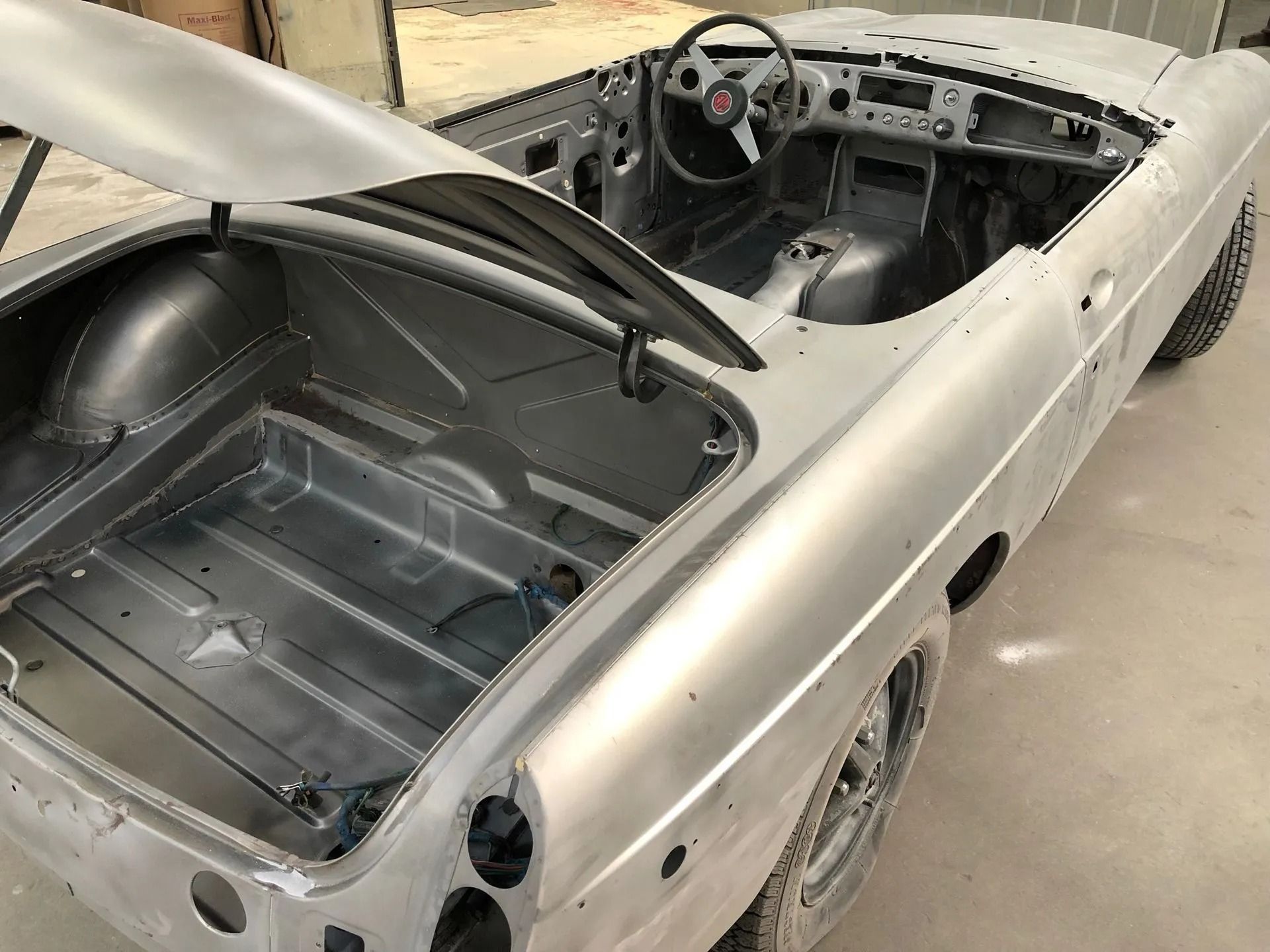 Bare metal classic convertible car undergoing restoration, with open hood and trunk.