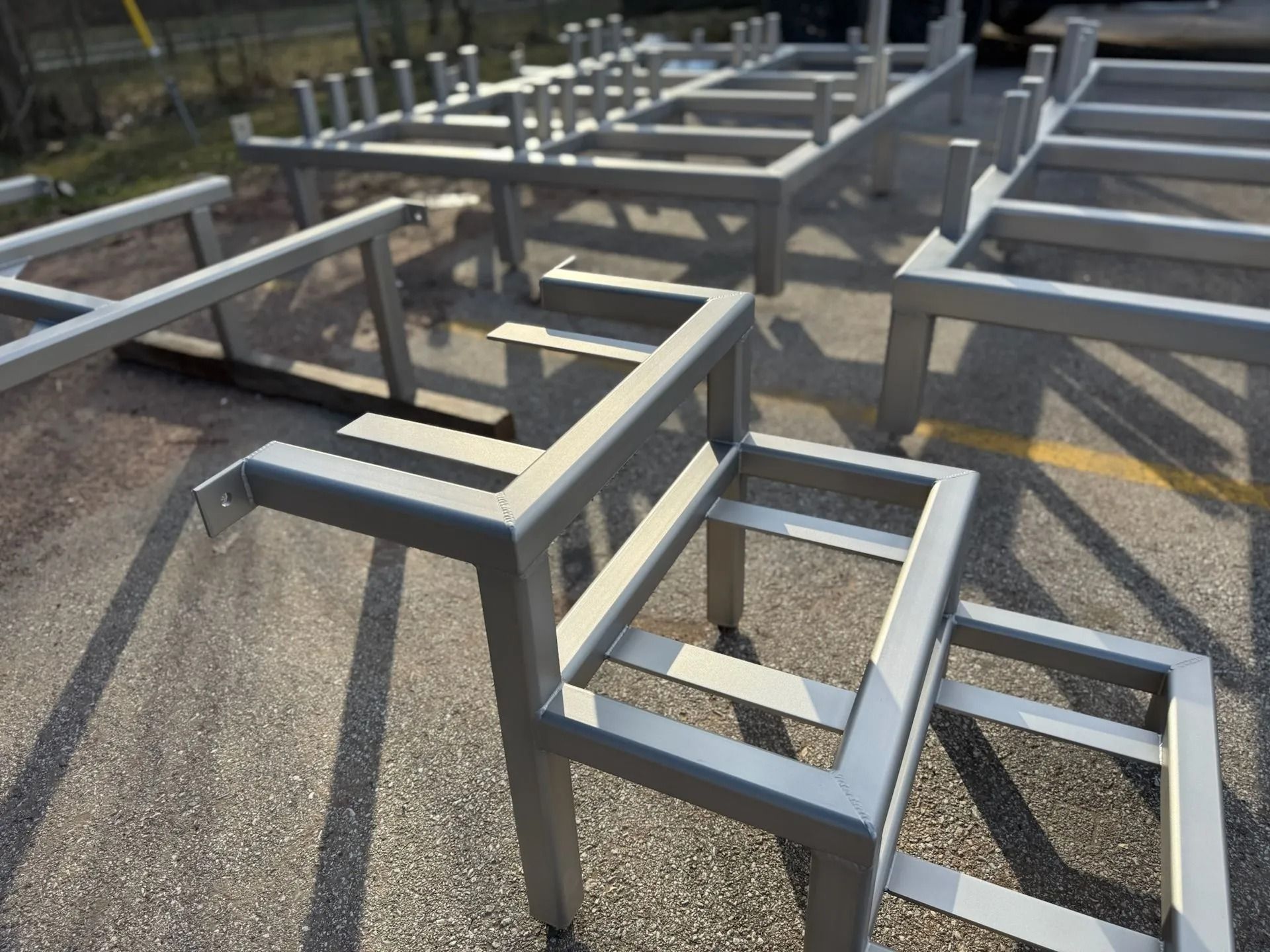 Metal frames, possibly for seating, in a parking lot. Grey, geometric structures.