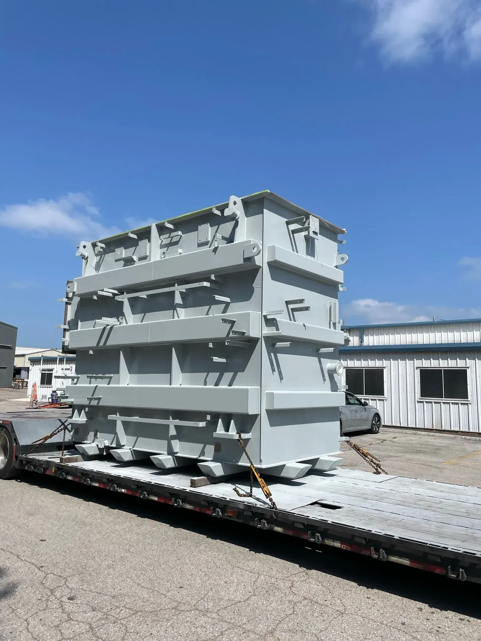 Large, gray industrial container secured on a flatbed trailer under a blue sky.