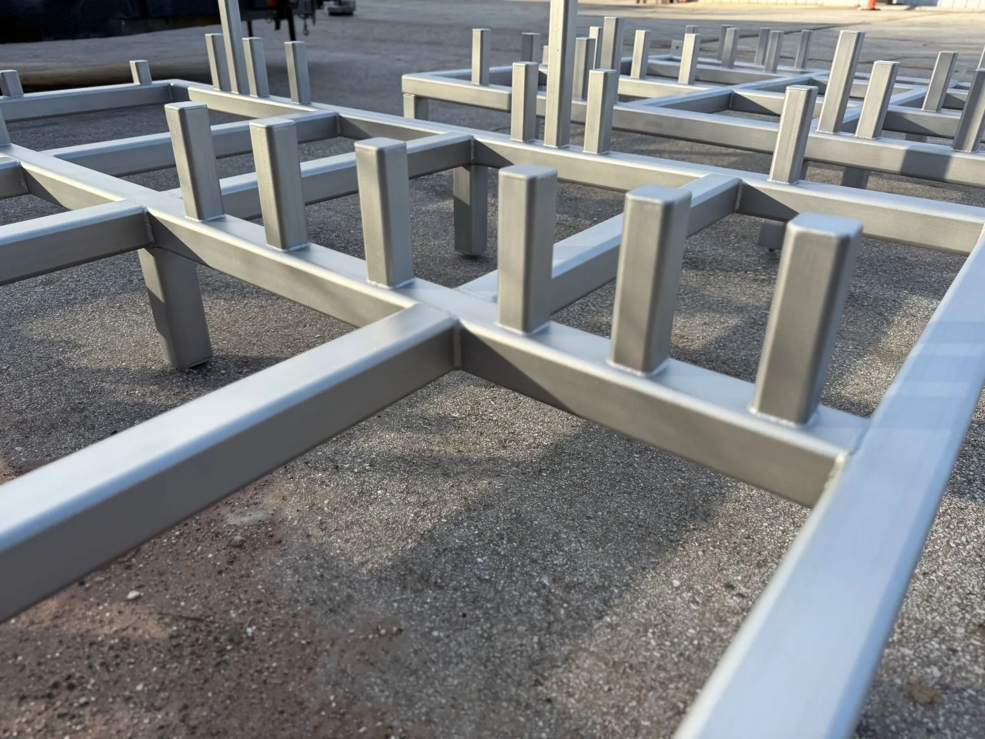 Silver metal rectangular framework with vertical posts on a gravel surface.