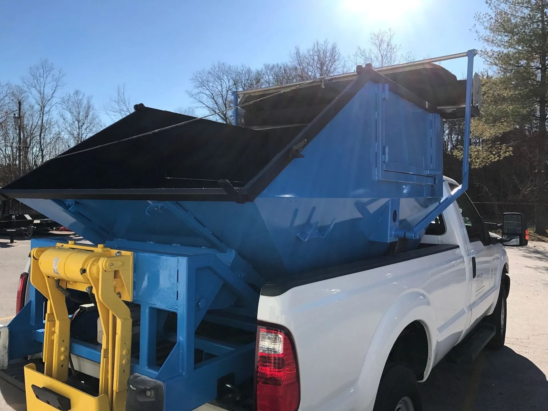 Blue salt spreader mounted on the back of a white pickup truck, used for road maintenance.