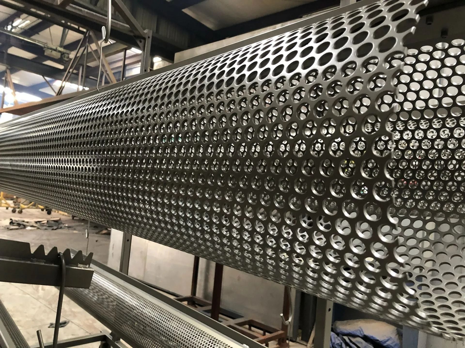 Perforated metal cylinder, possibly part of industrial equipment, in a factory setting.