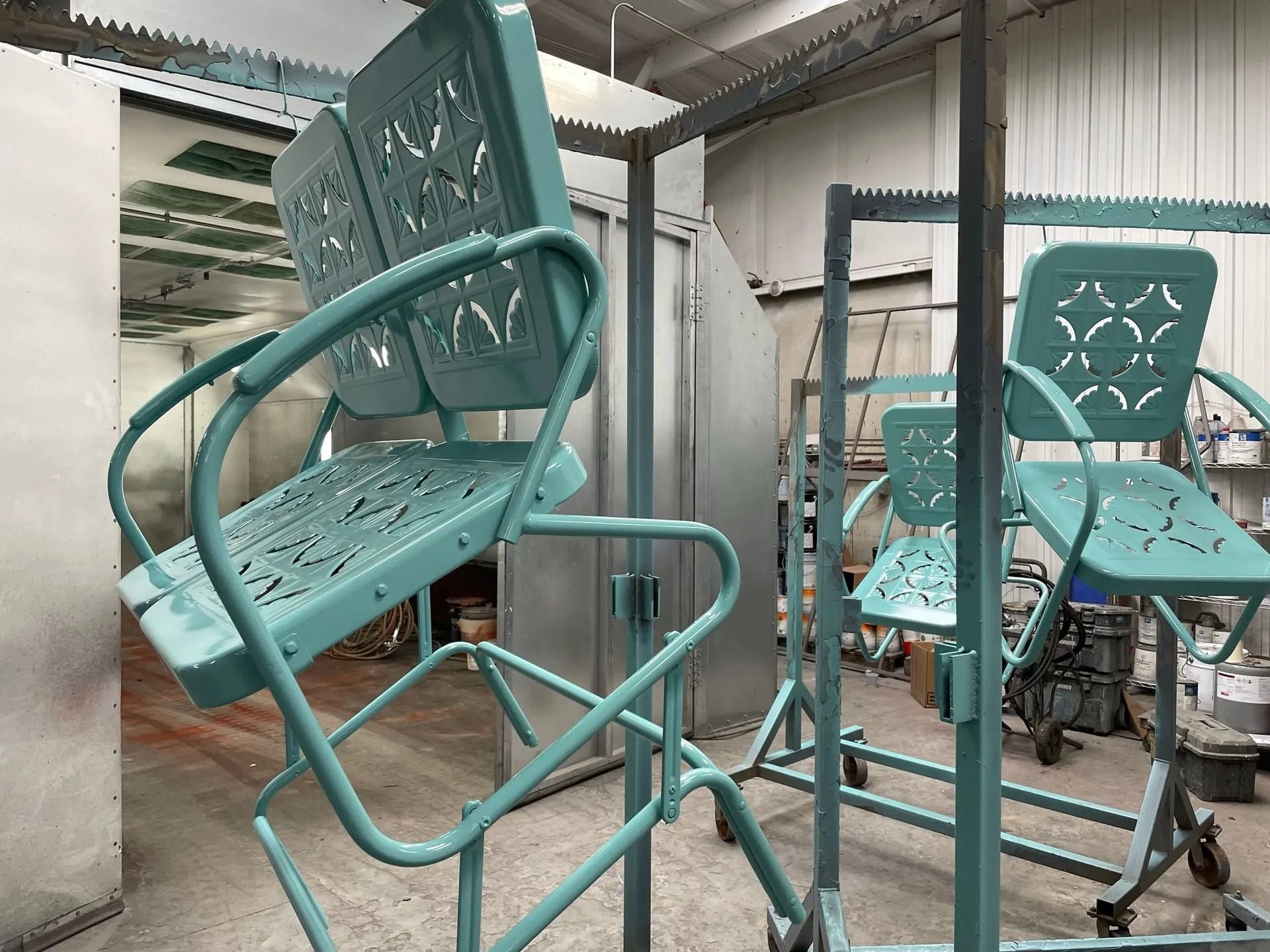 Teal metal patio chairs inside a spray painting booth.