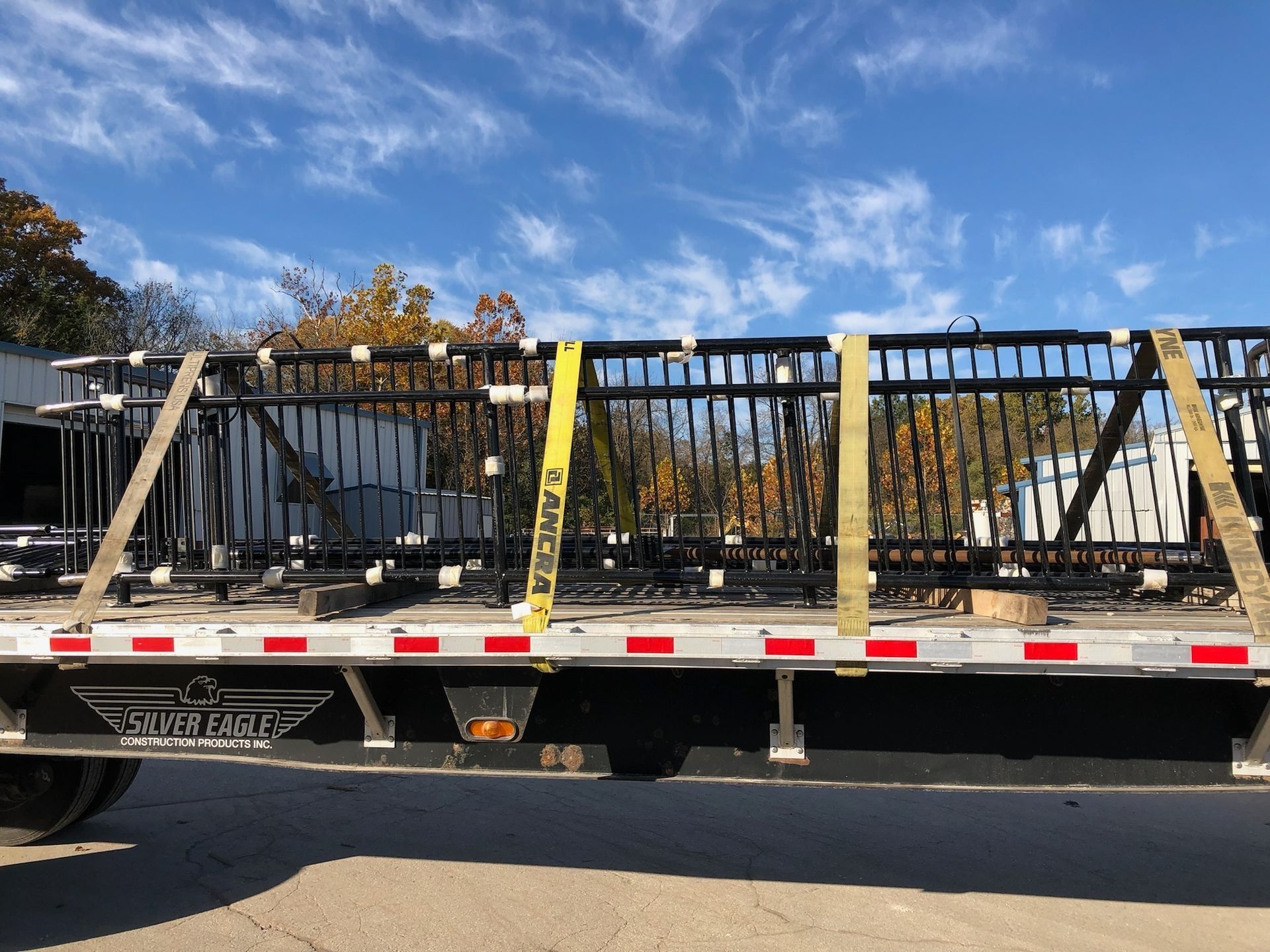 Black metal fence sections secured with straps on a flatbed truck against a blue sky.