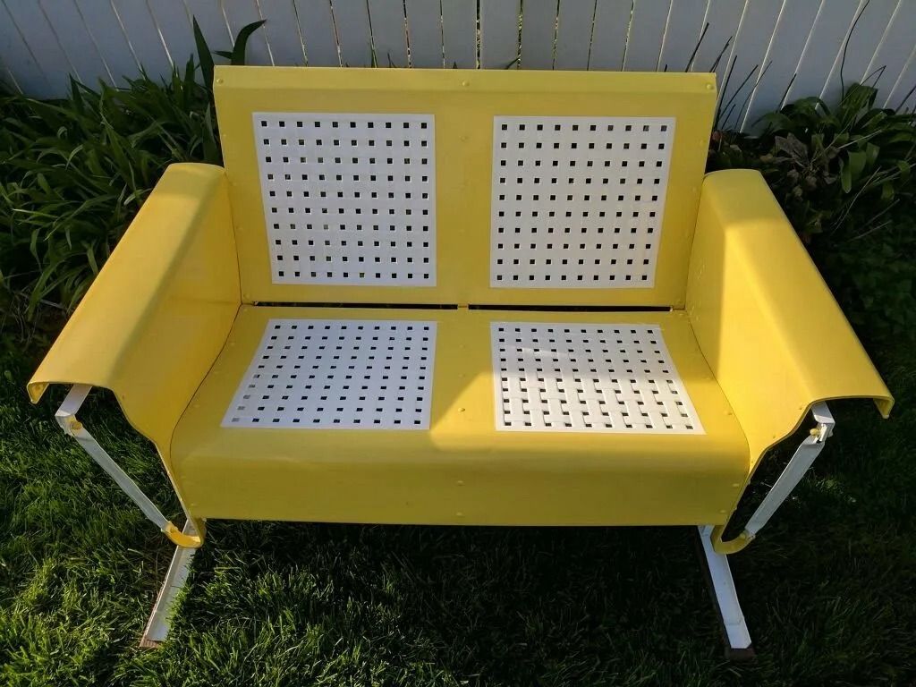 Yellow and white metal outdoor glider bench on green grass.