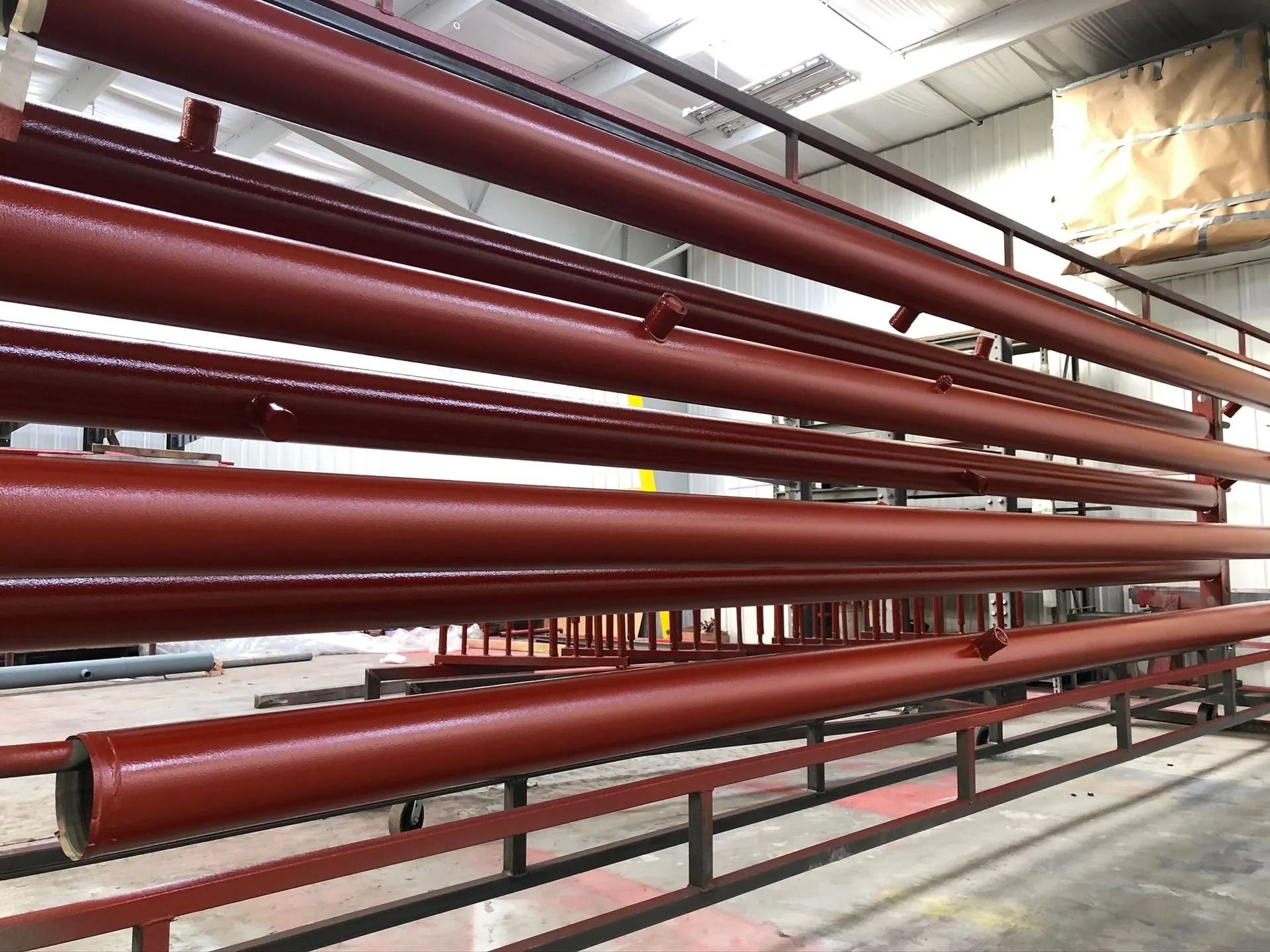 Red painted metal pipes on racks in a factory setting.