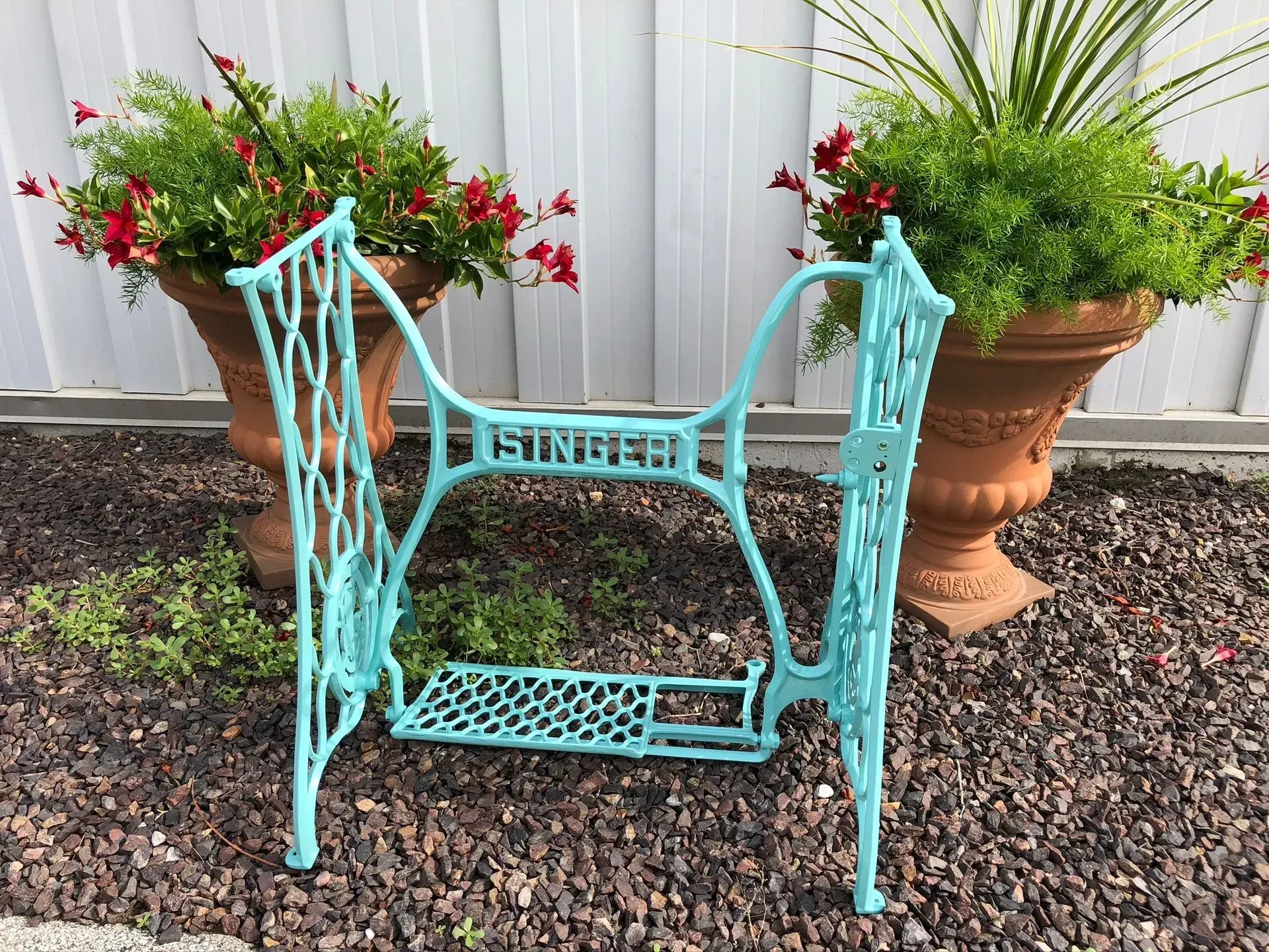 Turquoise Singer sewing machine base in front of potted flowers.