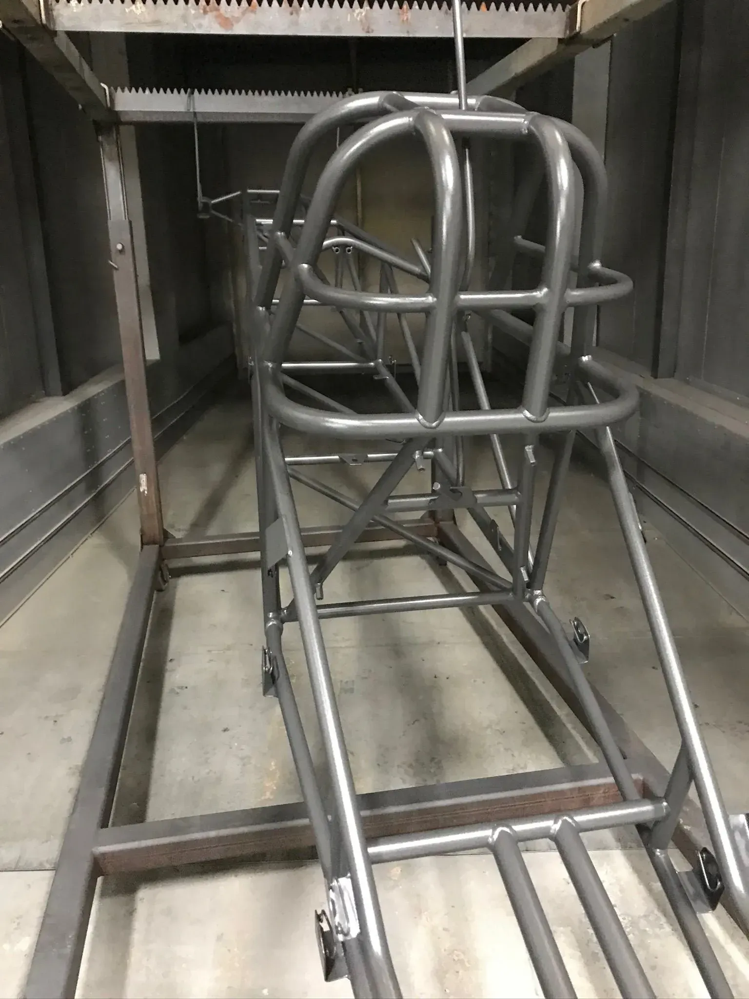 Gray race car chassis inside a spray booth.