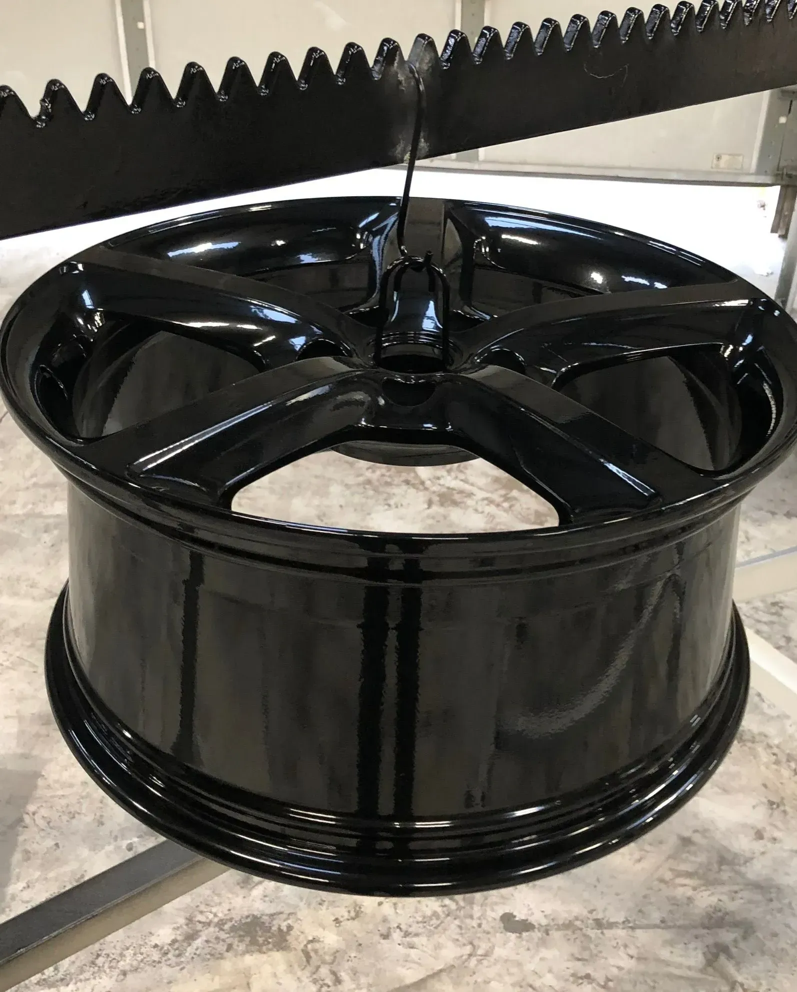 Black car wheel being coated with paint, hanging from a rack.