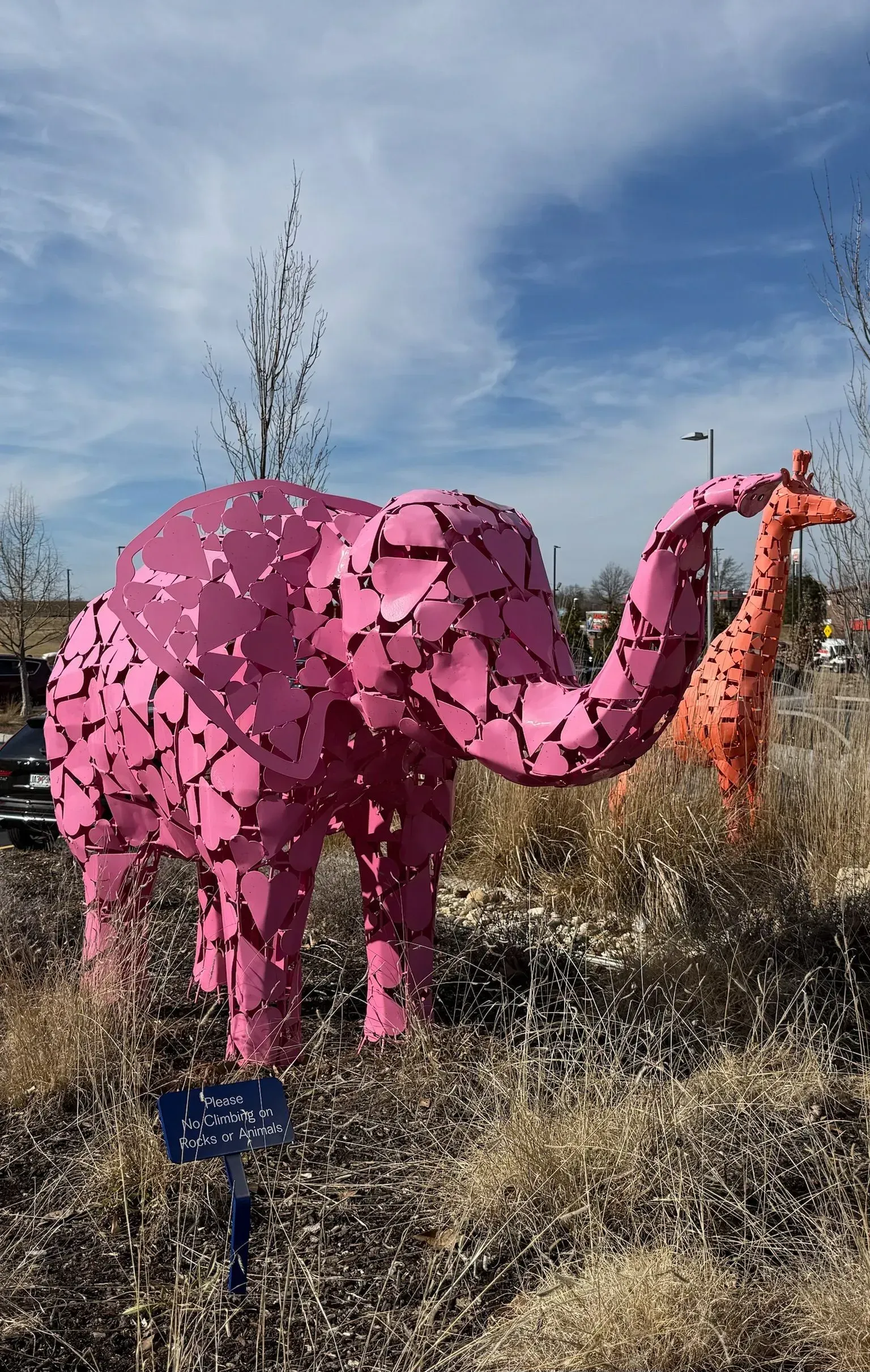Pink elephant sculpture with orange giraffe in a field under a blue sky.