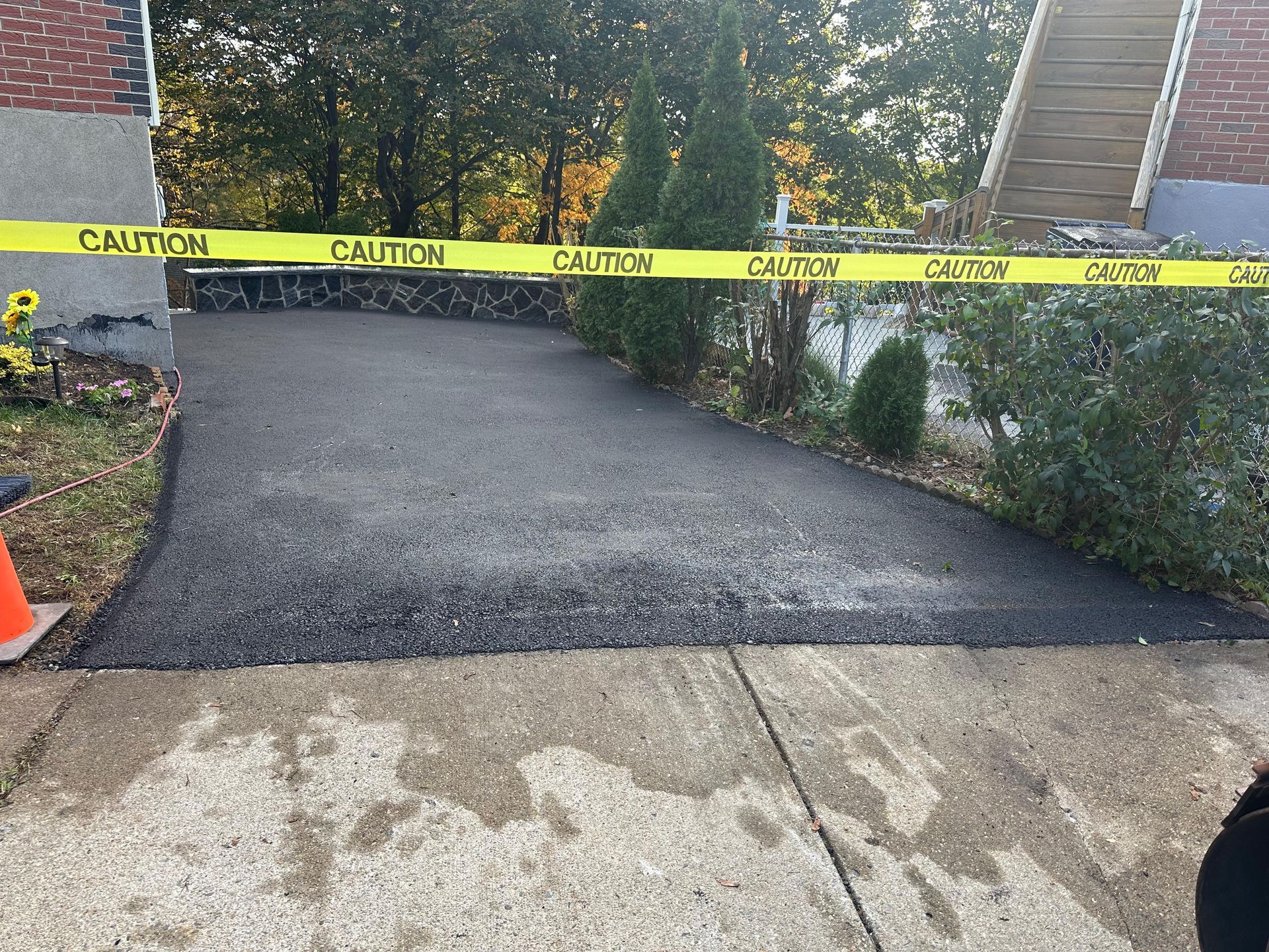 Caution tape blocking a newly paved driveway beside a sidewalk and hedges