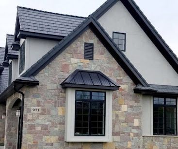 Stone-and-stucco house with dark shingled roof and front windows