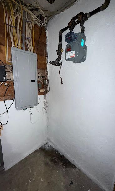 Electrical panel and exposed wiring in a small utility room with white walls and a concrete floor
