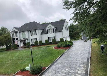 Suburban house with a long stone driveway, manicured lawn, and a child walking along the right side