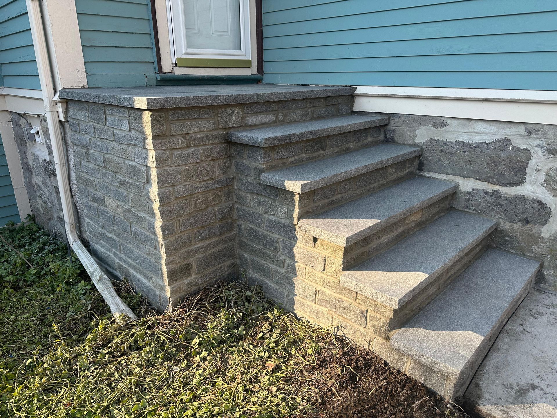 Outdoor stone-and-concrete front steps beside a house with blue siding and a stone foundation
