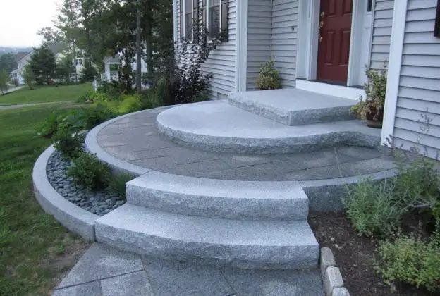 Three-tiered curved concrete front steps leading to a white house porch with siding and small shrubs