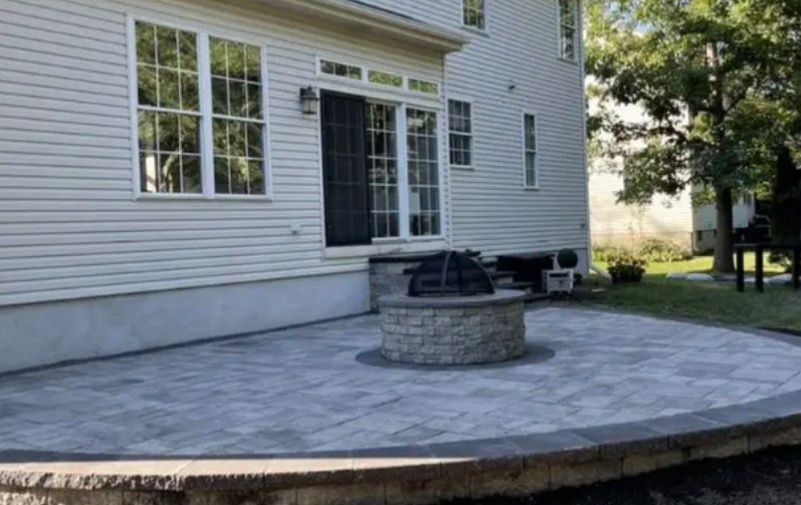 Backyard patio with a stone fire pit beside a white house and sliding glass door