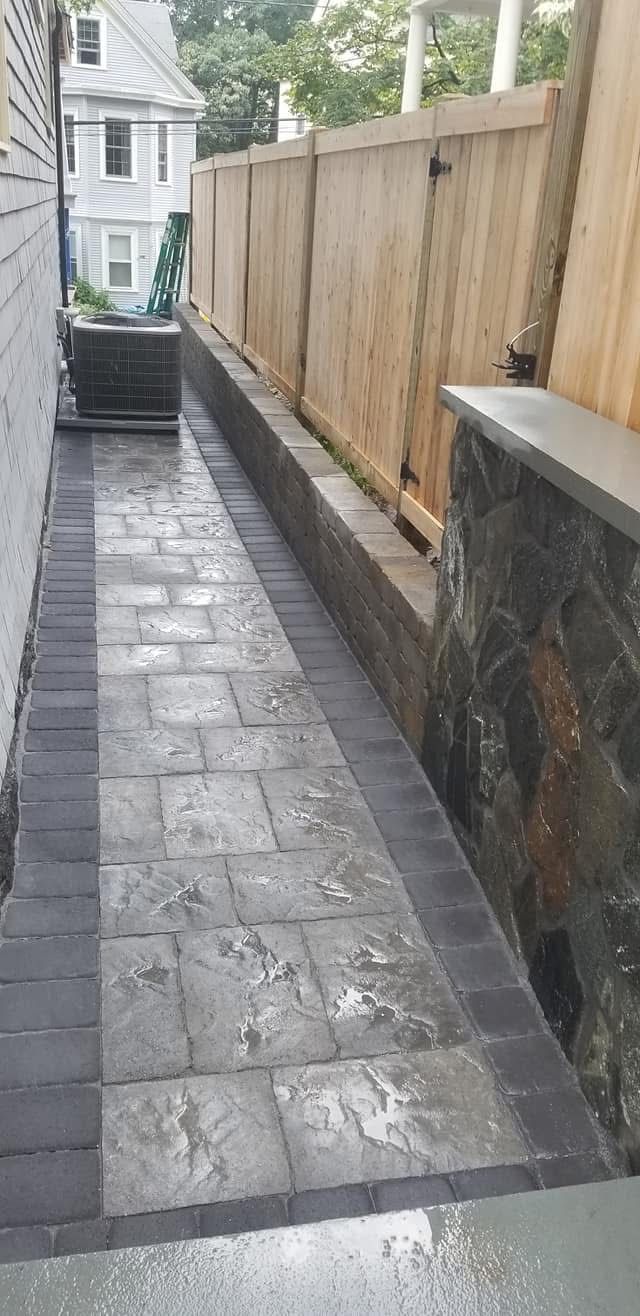 Narrow paved alley beside a house, with a wooden fence on the right and stone walls on both sides.