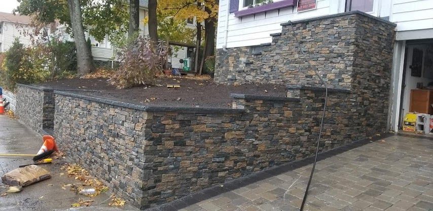 Stone-faced house with a raised retaining wall, paver driveway, and a worker at the left edge