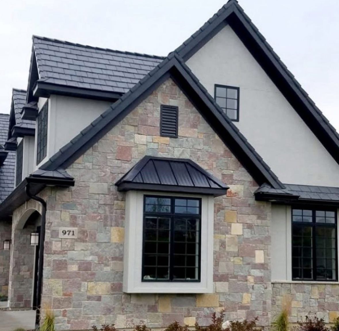 Stone-front house with dark gray roof, black-trimmed windows, and a small dormer above the entrance.