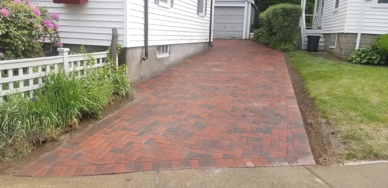 Brick-paved driveway between white houses with a flower bed and grass