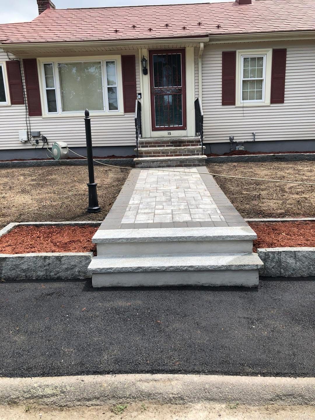 Front walkway and steps leading to a house entrance, with a tiled ramp and black handrail.