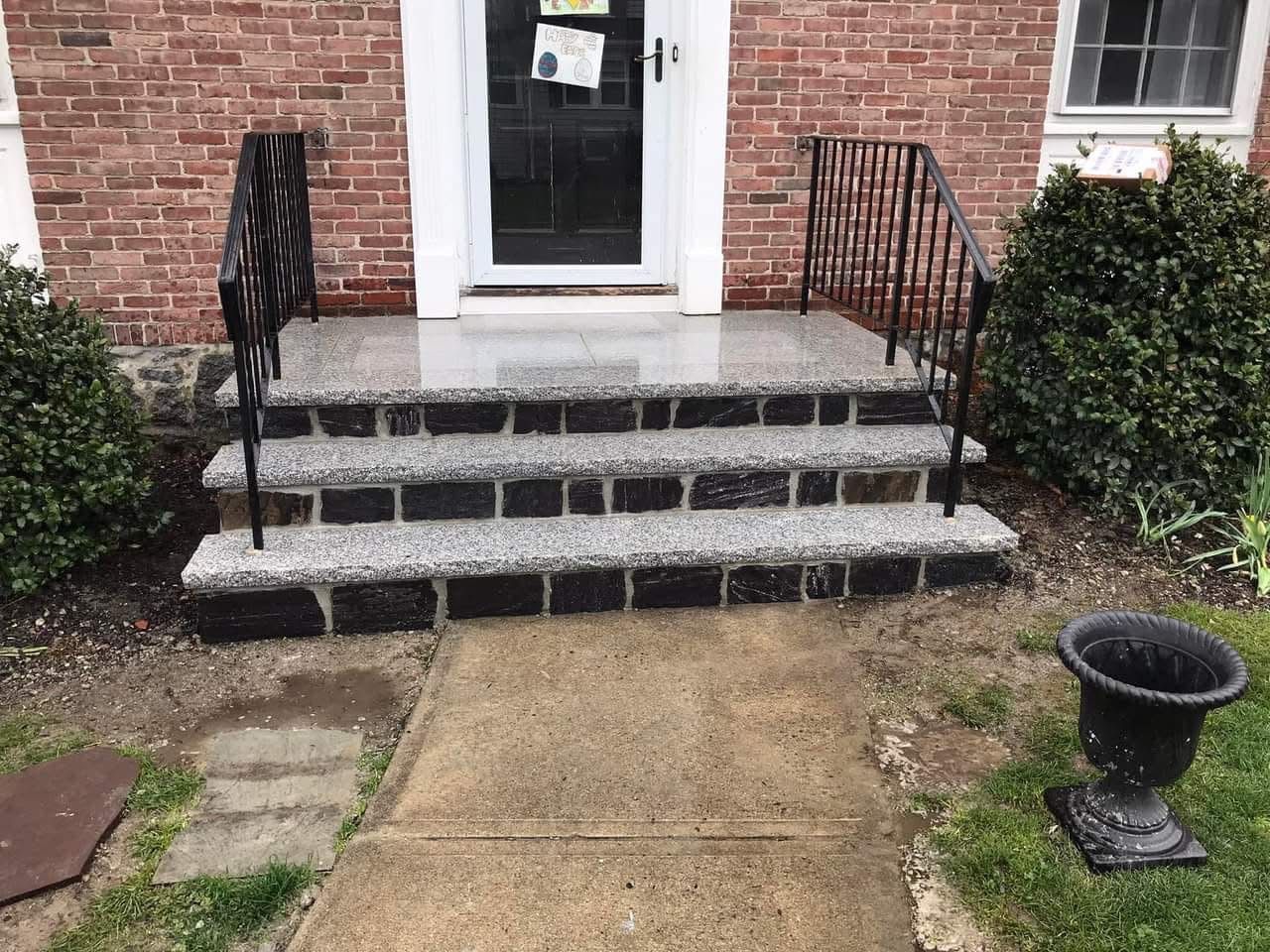 Brick house entry with stone steps, black railings, and a concrete walkway to the front door