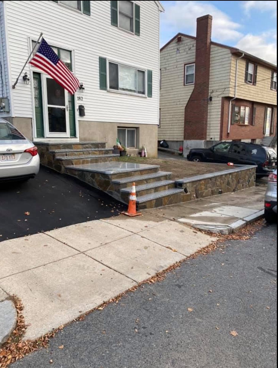 Residential entry with raised stone steps, an American flag, and parked cars on a street corner