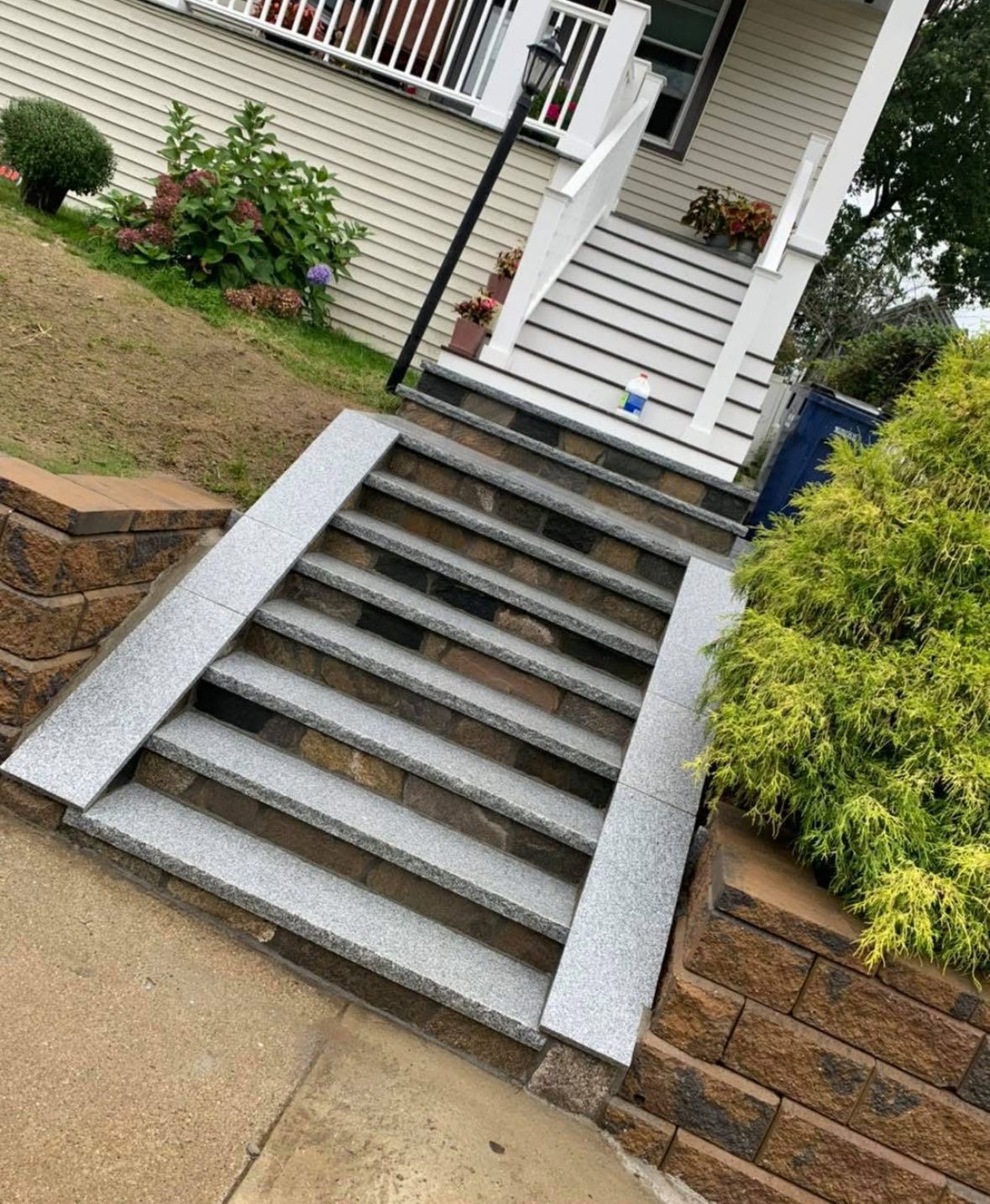 Concrete front steps leading to a house entrance, bordered by stone walls and garden landscaping