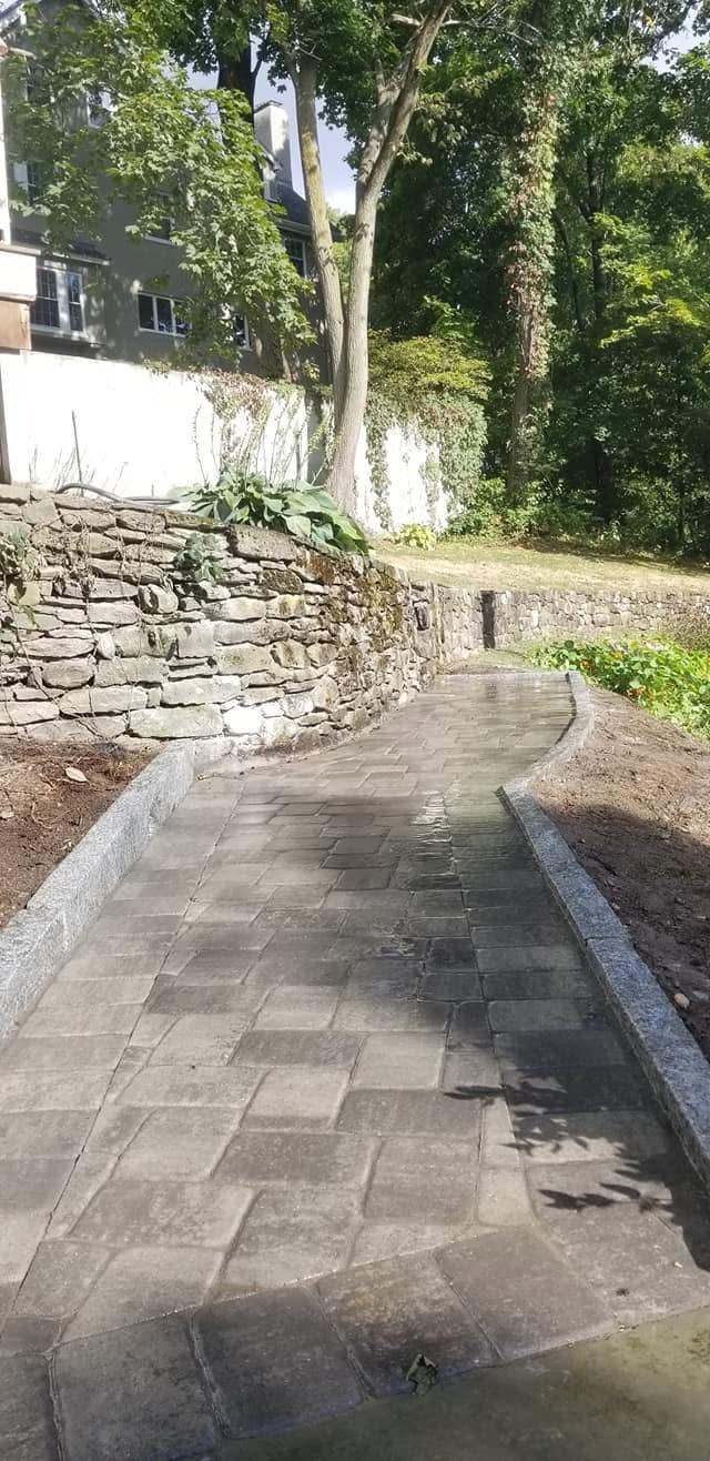 Curved stone walkway beside a low stone wall and trees in bright daylight