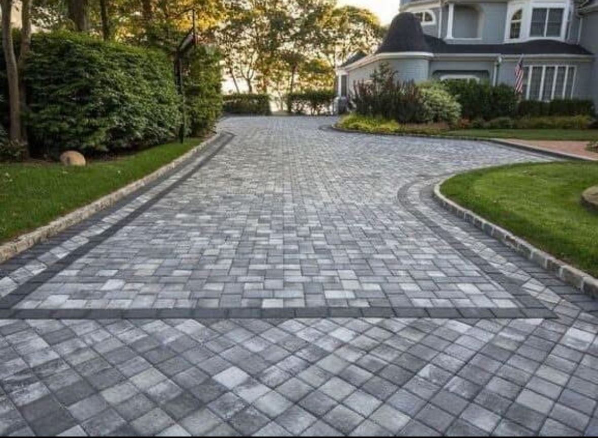 Stone-paved driveway leading to a house with green lawns and trees on both sides