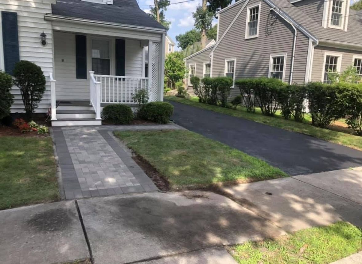 Small white house with front porch, stone walkway, and paved driveway beside a neighboring home.