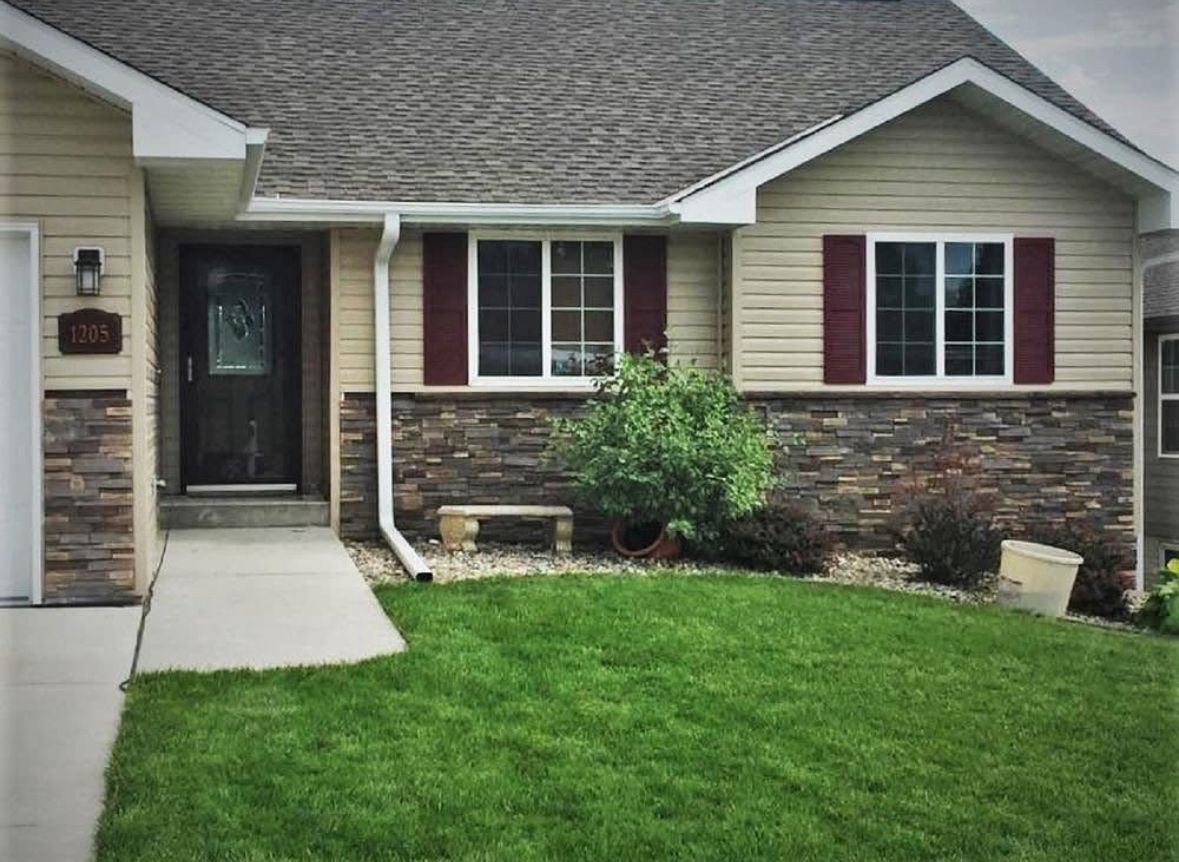 Suburban house exterior with beige siding, stone trim, maroon shutters, and a green lawn