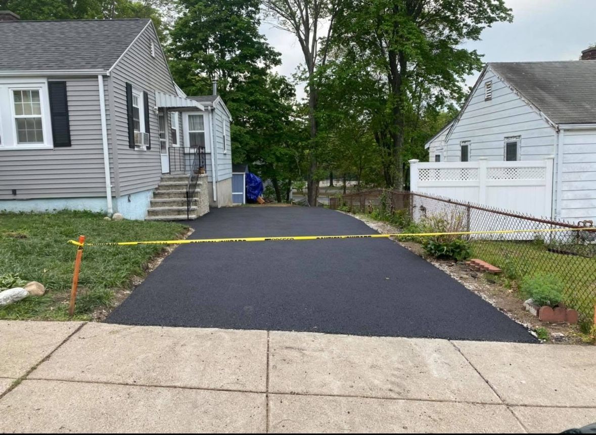 Freshly paved driveway between two houses, blocked by yellow caution tape at the street entrance