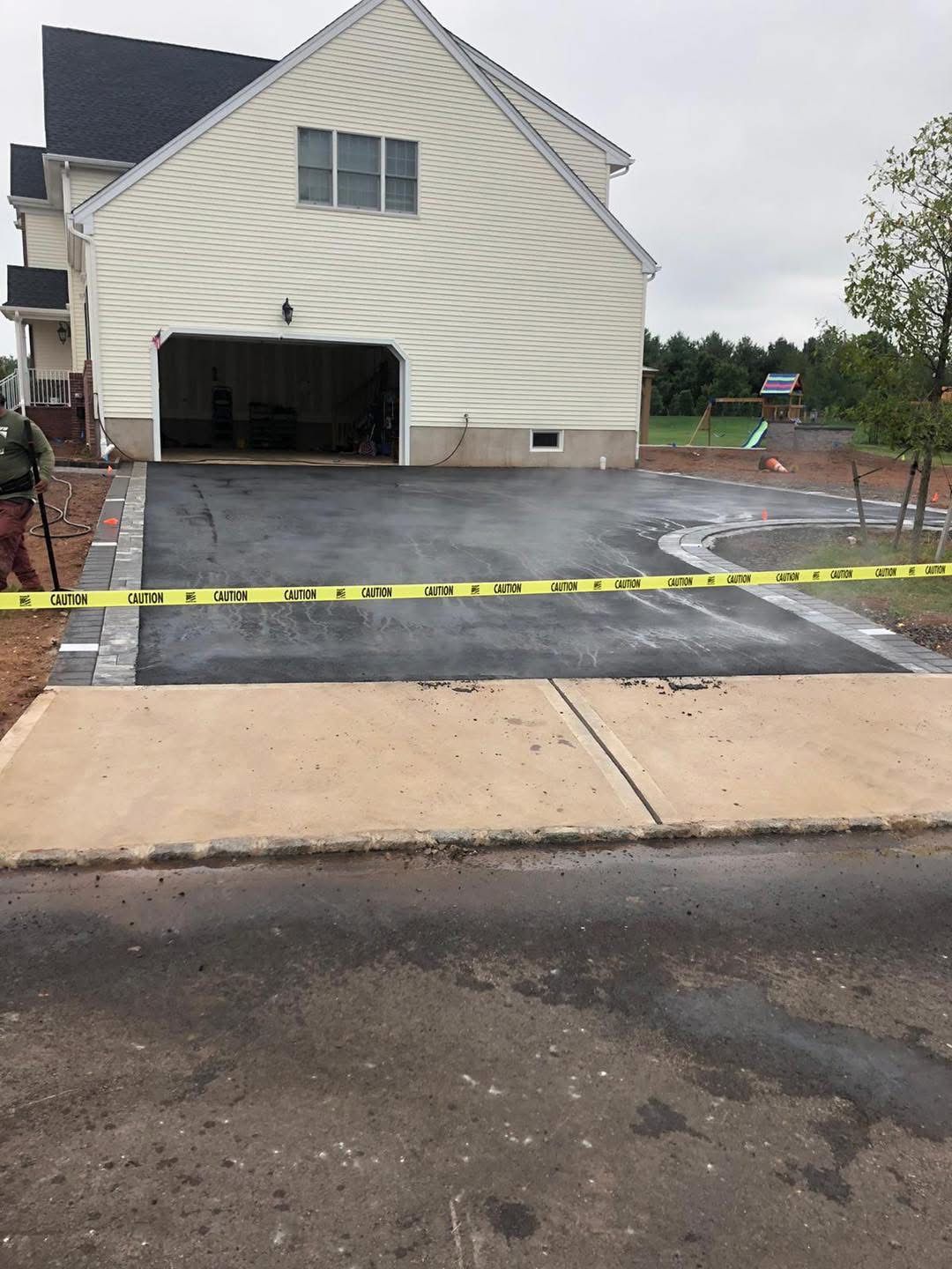 New driveway under construction in front of a beige house, with caution tape across the pavement.