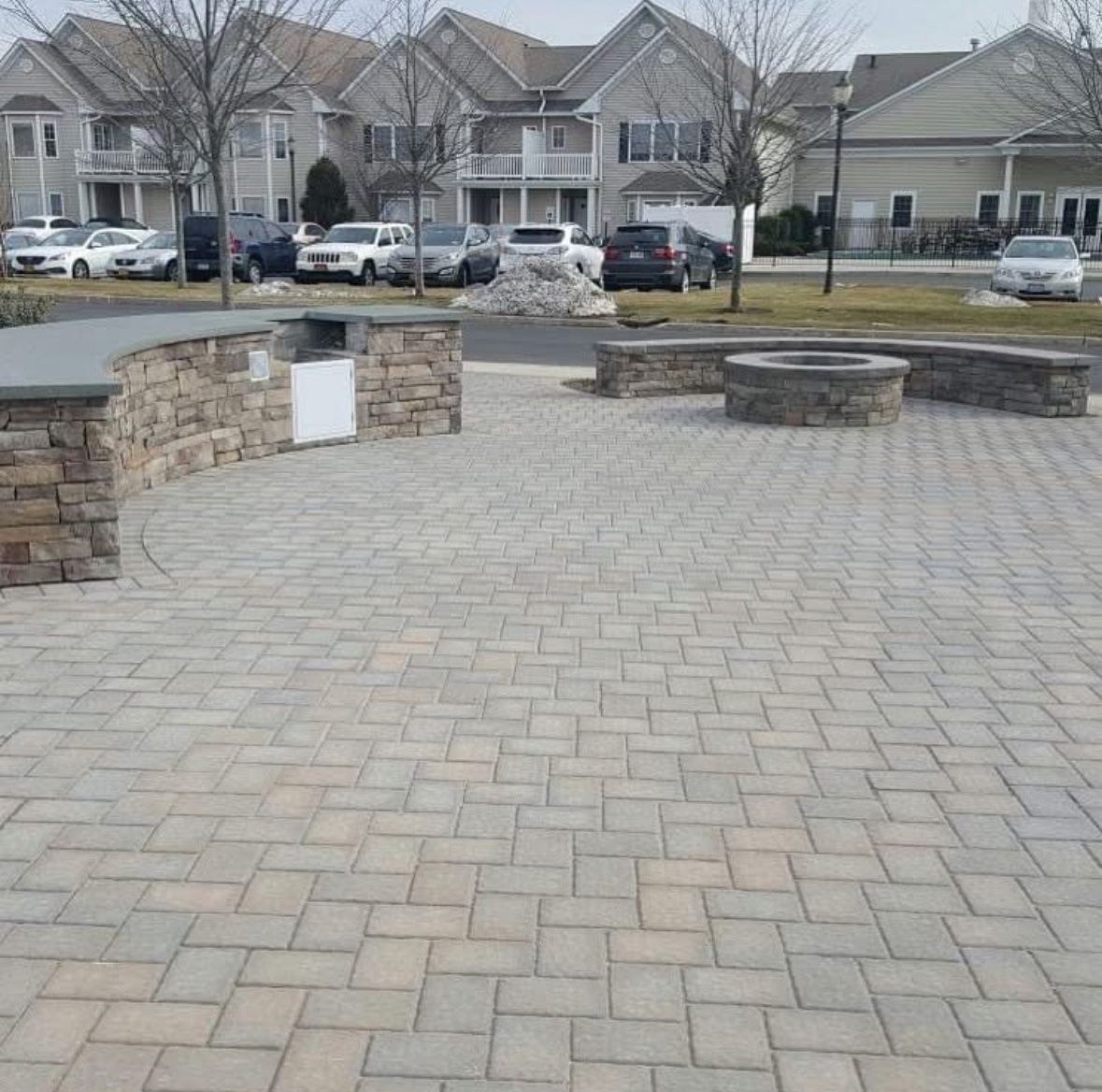 Brick-paved plaza with stone benches and low walls in front of suburban townhouses.