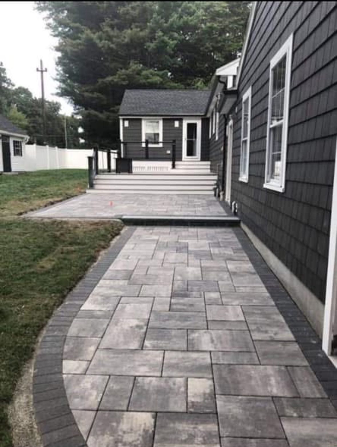 Paved stone walkway leading to a gray house with white trim and a small porch