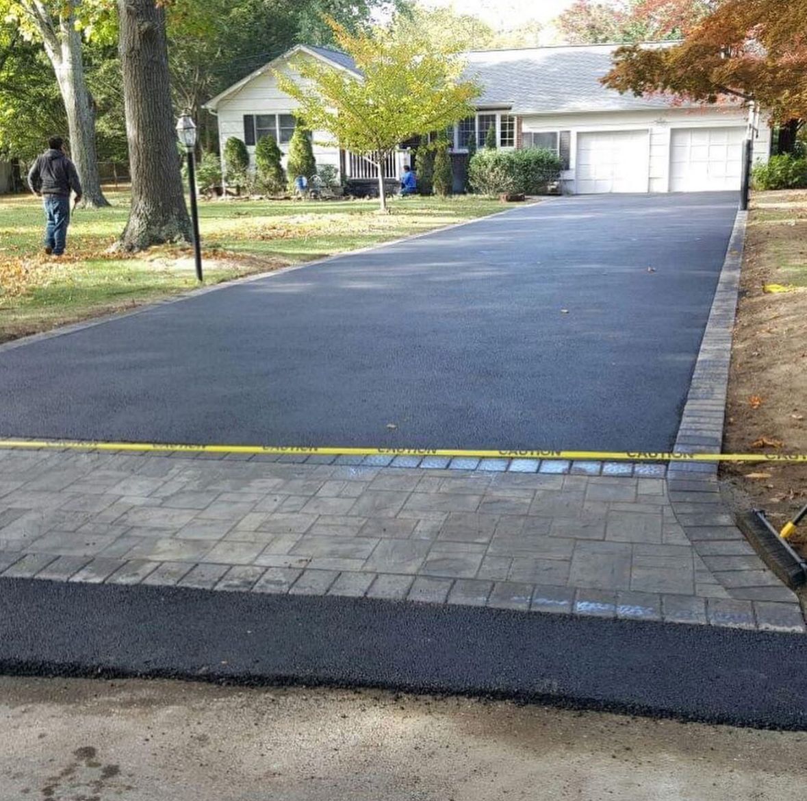 Freshly paved black driveway with paver apron in front of a suburban house