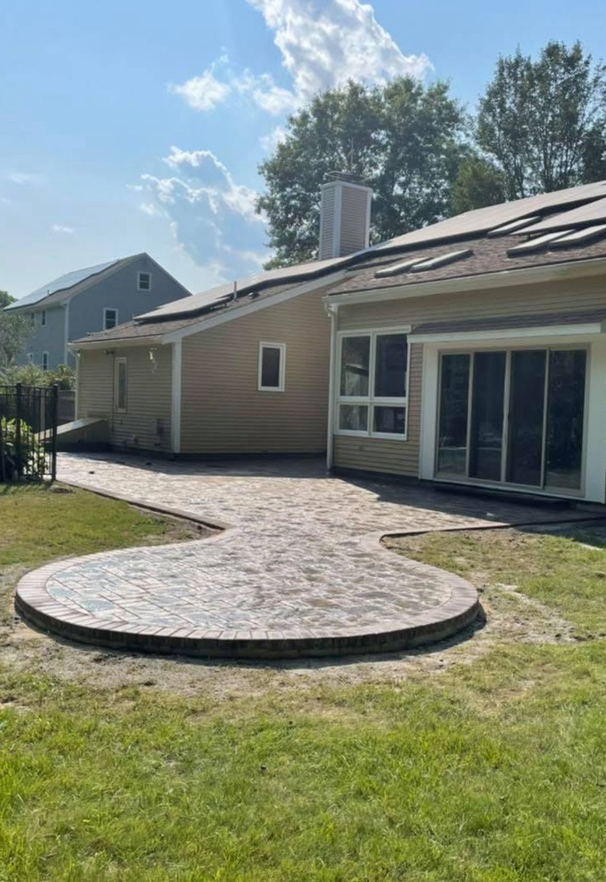 Backyard patio with circular stone paver area, sliding glass doors, and a house exterior under a blue sky