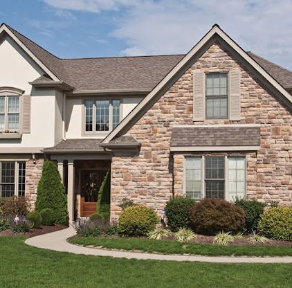 Suburban house with stone and beige siding, front porch, gabled roof, and landscaped lawn