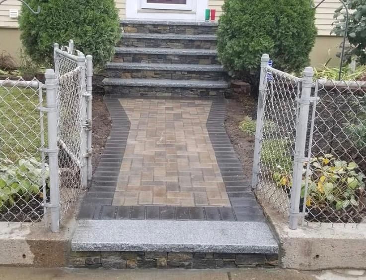 Front walkway with chain-link fence, brick path, and steps leading to a house entrance.