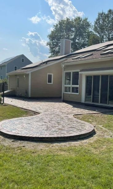 Backyard patio with curved paver walkway beside a beige house and sliding glass doors