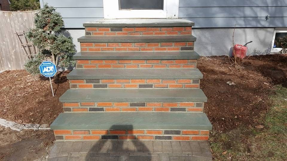 Brick steps leading to a front door, with mulched landscaping on both sides and a garden light on the left.